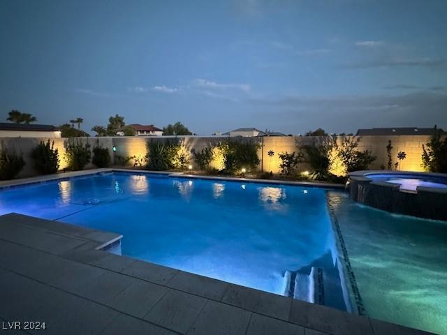 pool at dusk featuring an in ground hot tub and pool water feature