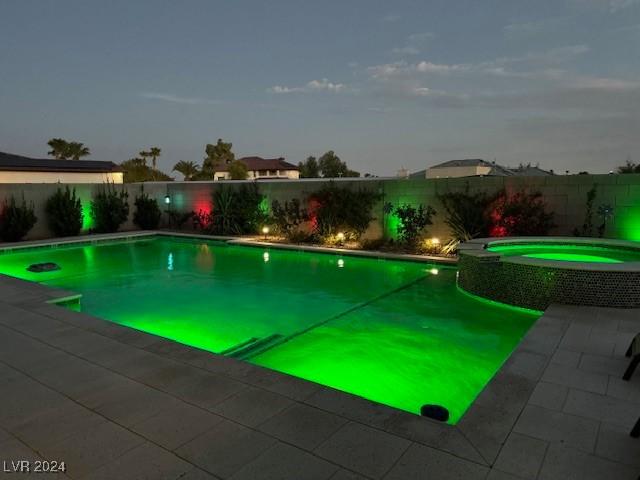 pool at dusk featuring an in ground hot tub