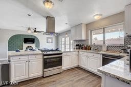 kitchen featuring white cabinets, stainless steel range oven, kitchen peninsula, wall chimney range hood, and light hardwood / wood-style flooring