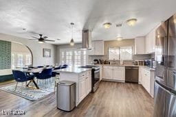 kitchen with light wood-type flooring, range hood, kitchen peninsula, appliances with stainless steel finishes, and white cabinetry