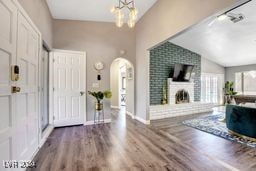 entrance foyer featuring a notable chandelier, hardwood / wood-style flooring, a fireplace, and vaulted ceiling