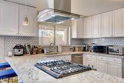 kitchen featuring stainless steel appliances, light stone countertops, range hood, and white cabinets