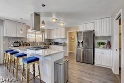 kitchen with wall chimney exhaust hood, light wood-type flooring, kitchen peninsula, white cabinets, and stainless steel fridge with ice dispenser