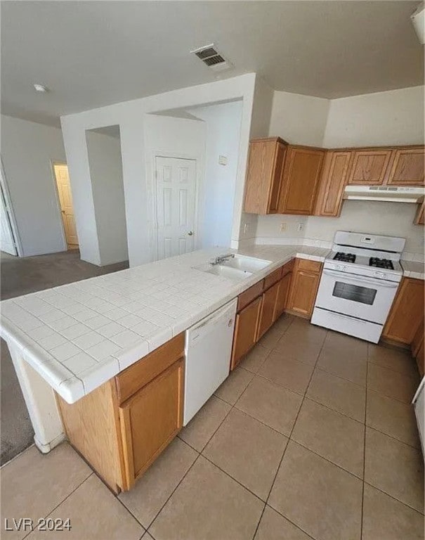 kitchen with light tile patterned floors, kitchen peninsula, sink, white appliances, and tile counters