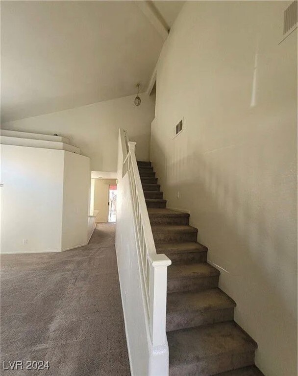 stairway with high vaulted ceiling and carpet floors