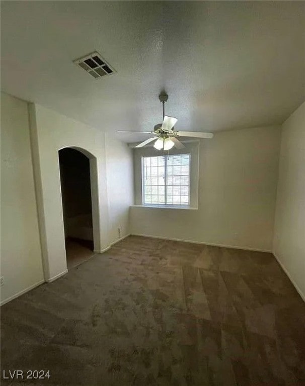 unfurnished room with ceiling fan, dark carpet, and a textured ceiling