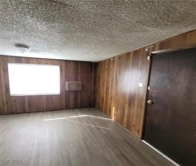 unfurnished room featuring wooden walls, wood-type flooring, and a textured ceiling