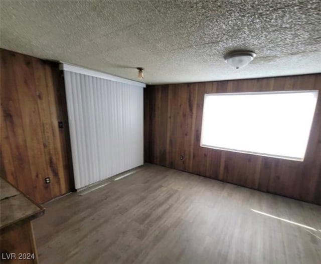 empty room featuring hardwood / wood-style flooring, wooden walls, and a textured ceiling