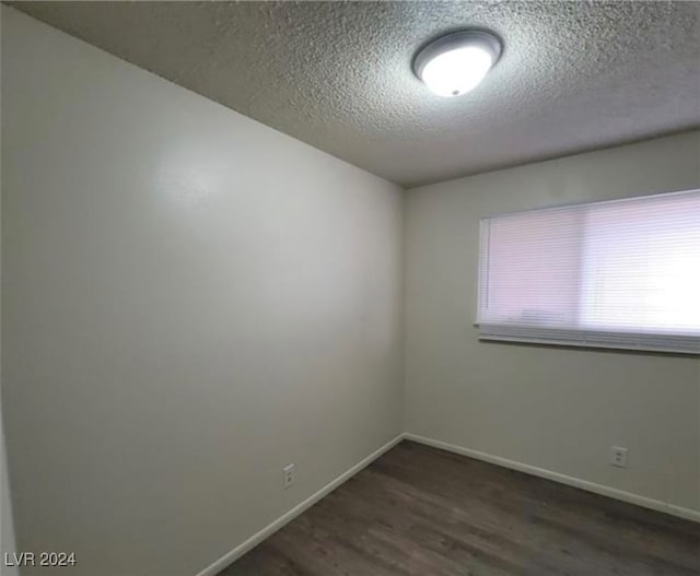 empty room with dark hardwood / wood-style floors, a wealth of natural light, and a textured ceiling