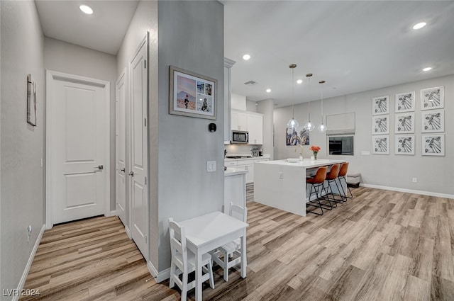 kitchen with light hardwood / wood-style floors, hanging light fixtures, white cabinetry, and a kitchen island with sink