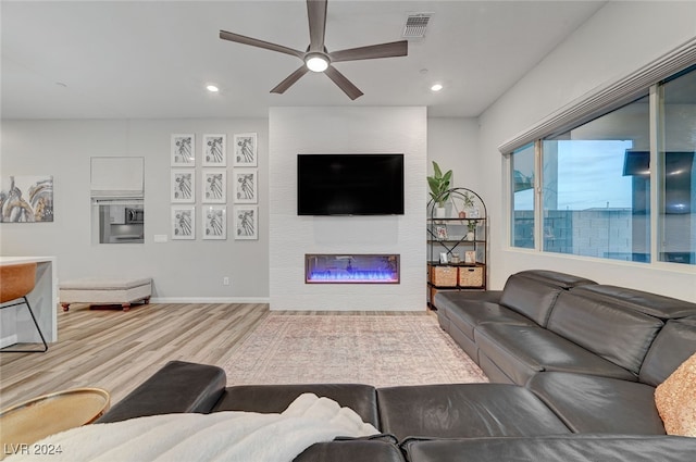 living room featuring ceiling fan, light wood-type flooring, and a large fireplace