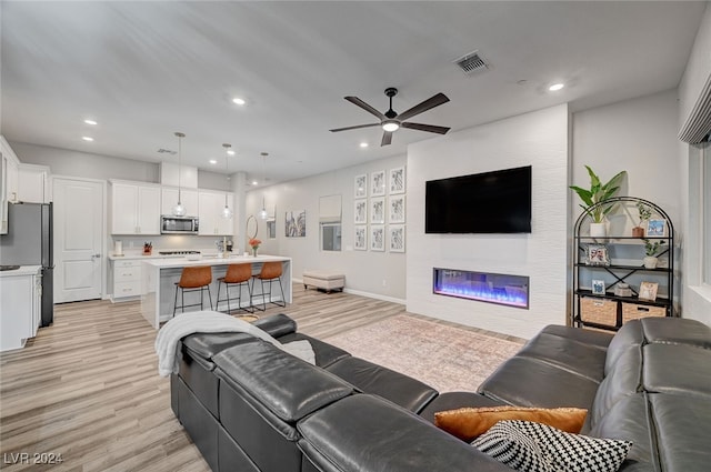 living room with light wood-type flooring, a fireplace, and ceiling fan