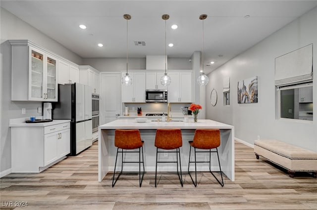 kitchen with light wood-type flooring, pendant lighting, a center island with sink, stainless steel appliances, and white cabinetry