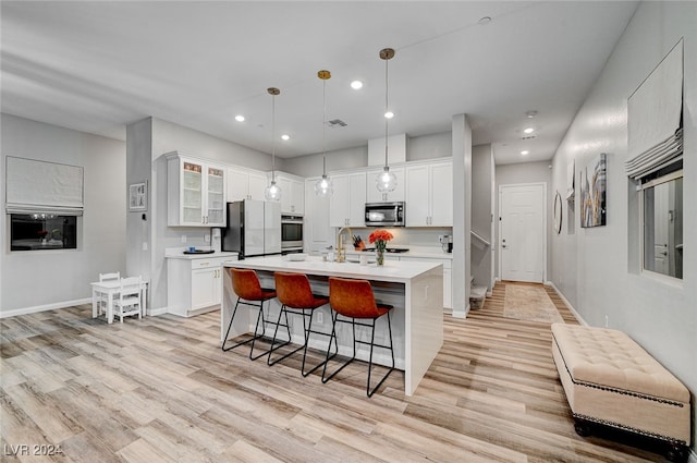 kitchen featuring pendant lighting, light hardwood / wood-style flooring, an island with sink, white cabinets, and appliances with stainless steel finishes