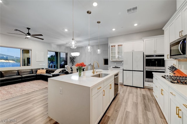 kitchen with an island with sink, white cabinets, sink, hanging light fixtures, and appliances with stainless steel finishes