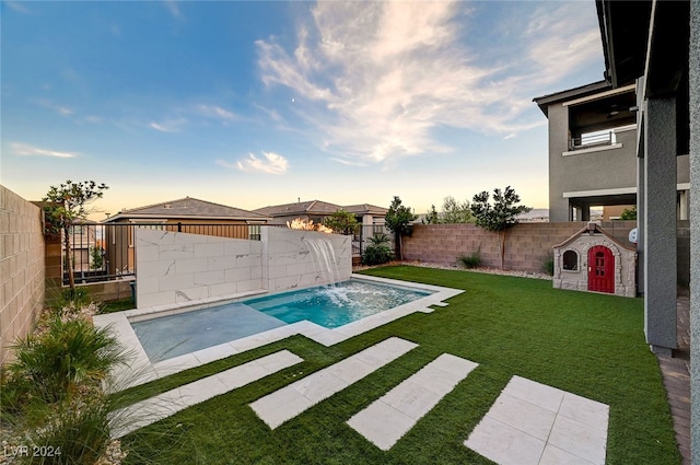 pool at dusk featuring pool water feature and a lawn