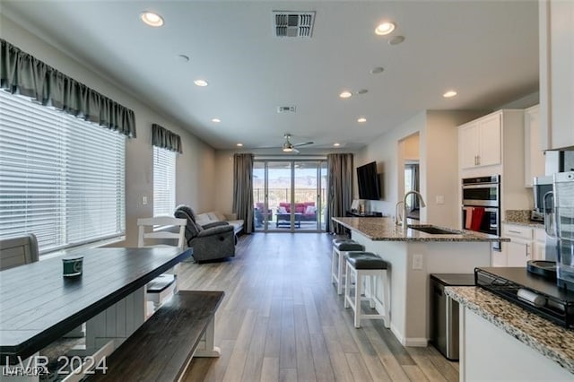 kitchen with double oven, an island with sink, light hardwood / wood-style flooring, and white cabinetry