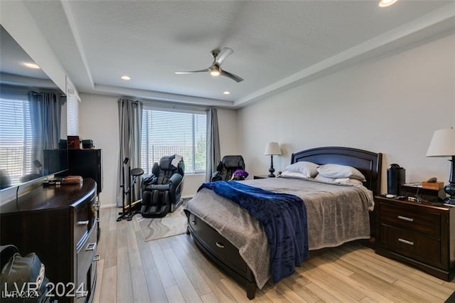 bedroom with ceiling fan, a tray ceiling, light hardwood / wood-style floors, and multiple windows