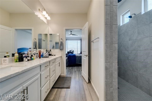 bathroom with wood-type flooring, a tile shower, vanity, and ceiling fan