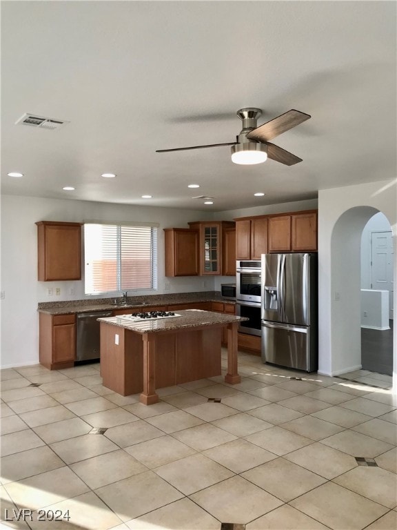 kitchen with a kitchen island, ceiling fan, stainless steel appliances, dark stone counters, and a kitchen breakfast bar