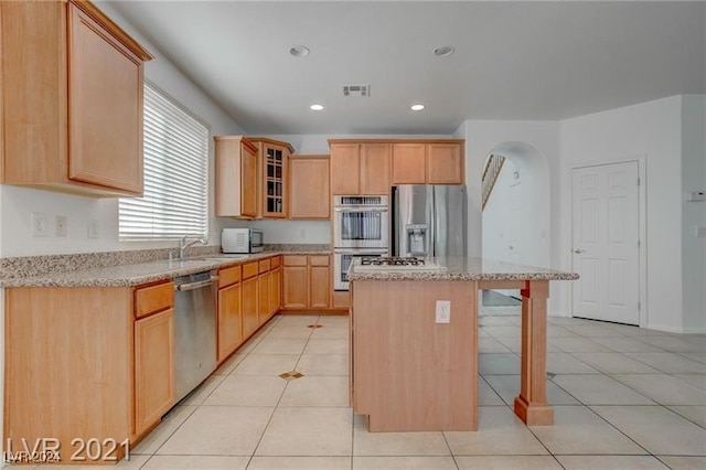 kitchen featuring light brown cabinetry, a kitchen island, stainless steel appliances, light stone countertops, and light tile patterned floors