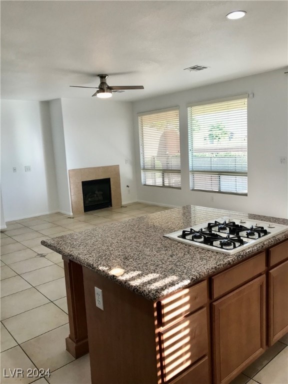 kitchen featuring ceiling fan, light tile patterned floors, stone counters, a tile fireplace, and white gas stovetop