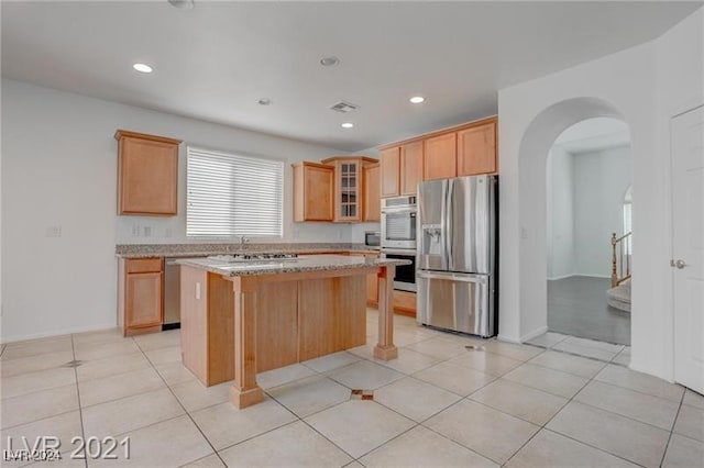 kitchen with light tile patterned floors, appliances with stainless steel finishes, a center island, a breakfast bar area, and light stone countertops