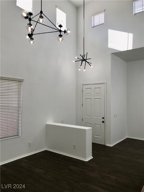 unfurnished room featuring a towering ceiling, a chandelier, and dark hardwood / wood-style flooring