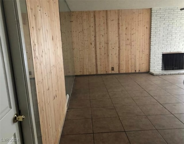 tiled empty room featuring a brick fireplace and wood walls