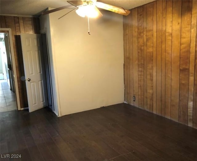 spare room featuring dark hardwood / wood-style flooring, wooden walls, and ceiling fan