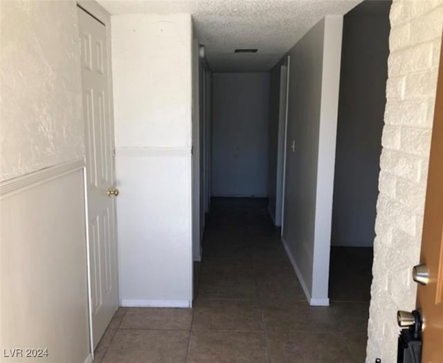 hallway featuring a textured ceiling and dark tile patterned flooring