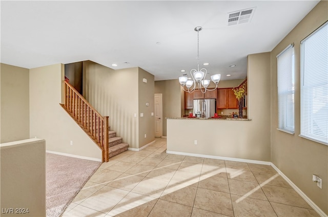 kitchen featuring light stone counters, stainless steel fridge, light tile patterned floors, kitchen peninsula, and a notable chandelier