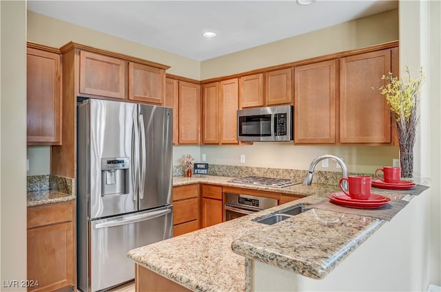 kitchen featuring appliances with stainless steel finishes, kitchen peninsula, light stone counters, and sink