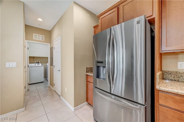 kitchen with light stone countertops, washer / clothes dryer, stainless steel refrigerator with ice dispenser, and light tile patterned floors