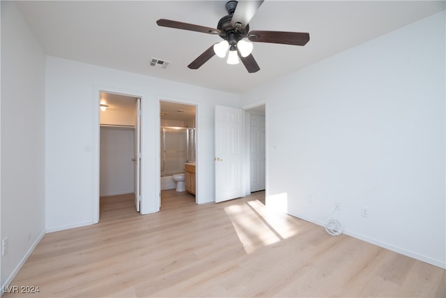 unfurnished bedroom featuring ceiling fan, light wood-type flooring, ensuite bath, and a spacious closet