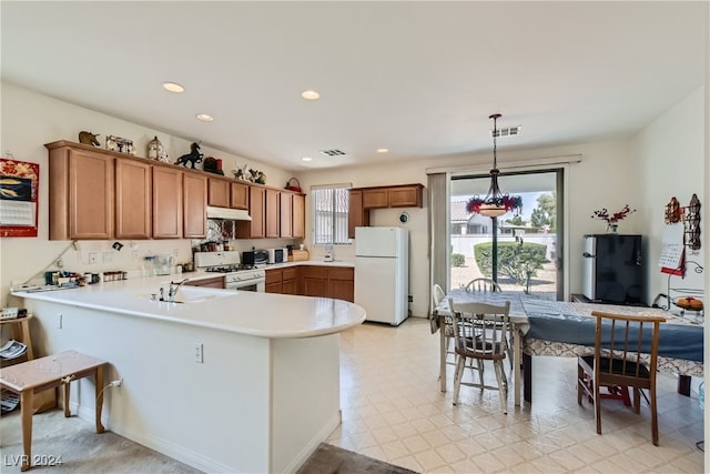 kitchen featuring pendant lighting, white appliances, sink, and kitchen peninsula