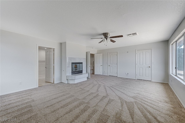 unfurnished living room featuring light carpet, a fireplace, ceiling fan, and a textured ceiling