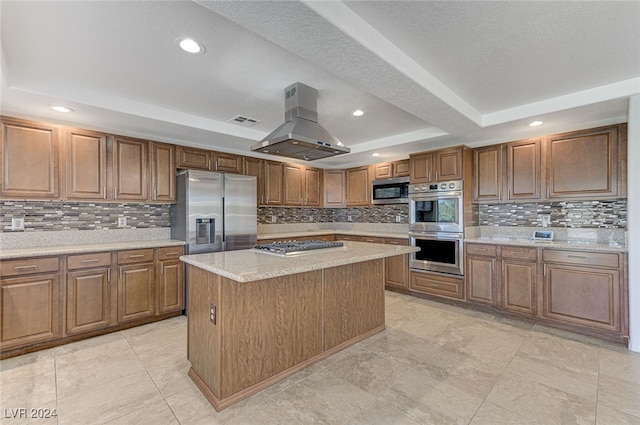 kitchen with island range hood, appliances with stainless steel finishes, a tray ceiling, a center island, and decorative backsplash