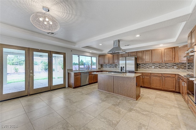 kitchen with ventilation hood, a raised ceiling, hanging light fixtures, appliances with stainless steel finishes, and a center island