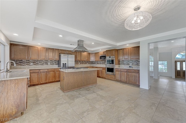 kitchen with sink, a kitchen island, island exhaust hood, appliances with stainless steel finishes, and a notable chandelier