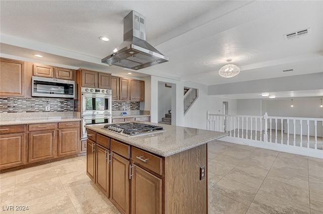 kitchen with light stone counters, island exhaust hood, appliances with stainless steel finishes, a center island, and decorative backsplash