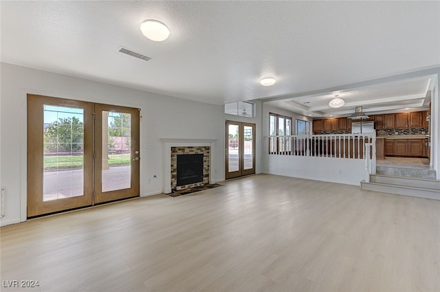 unfurnished living room with plenty of natural light, french doors, light hardwood / wood-style flooring, and a textured ceiling