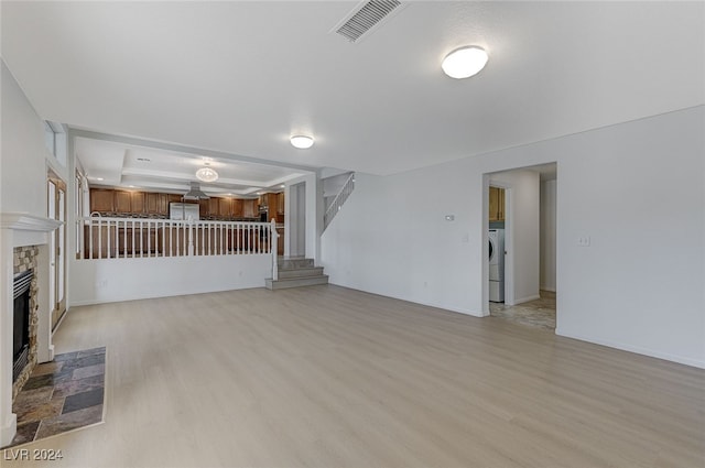 unfurnished living room featuring washer / dryer, a stone fireplace, and light hardwood / wood-style floors