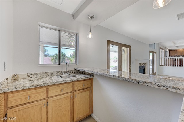 kitchen featuring light stone countertops, light brown cabinets, sink, kitchen peninsula, and pendant lighting