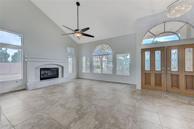 unfurnished living room with light tile patterned flooring, ceiling fan with notable chandelier, a premium fireplace, and high vaulted ceiling