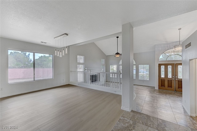 unfurnished living room featuring ceiling fan with notable chandelier, hardwood / wood-style flooring, lofted ceiling, and a textured ceiling