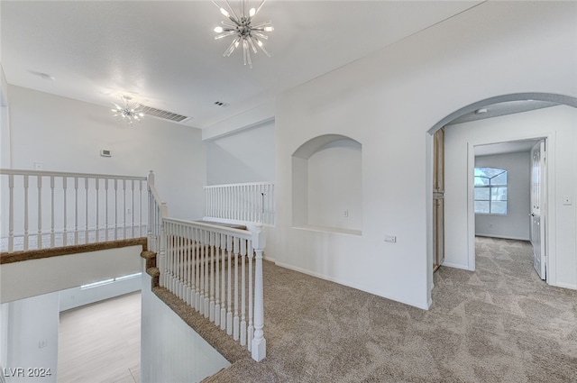 hall with light colored carpet and a notable chandelier