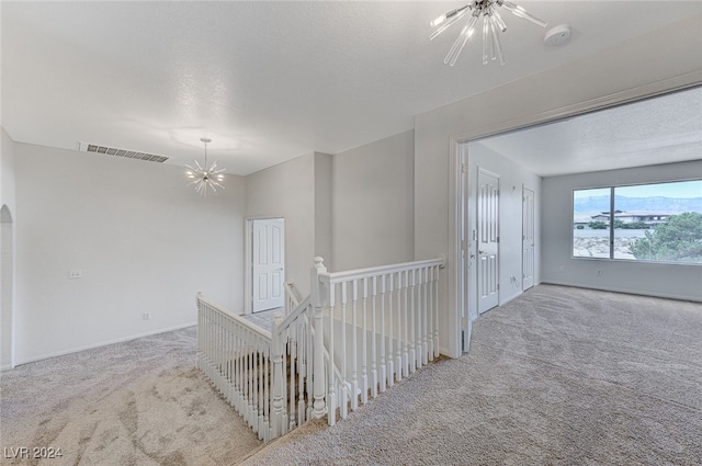 hallway with light carpet, an inviting chandelier, and a textured ceiling