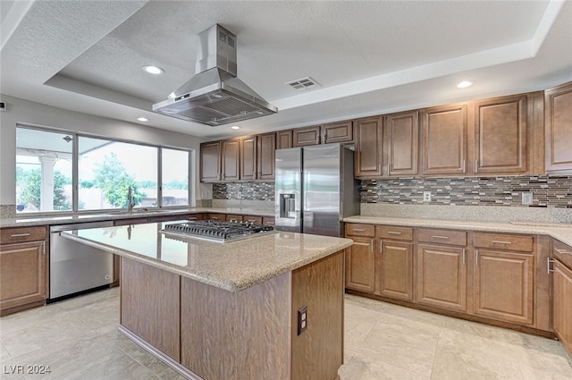 kitchen featuring range hood, appliances with stainless steel finishes, a center island, and a tray ceiling