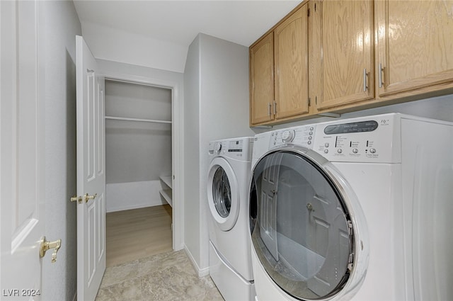 laundry room with washing machine and clothes dryer, light hardwood / wood-style floors, and cabinets